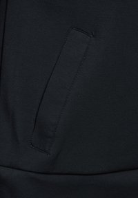 Felpa nera in tessuto con tasca verticale sul lato sinistro, texture liscia e dettagli di cucitura minimi.