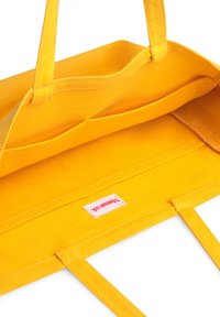 Gul canvas shoppingväska med två kraftiga handtag, öppen insida och en vävd etikett eller tagg synlig längst ner.