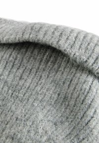 Tissu en laine tricotée grise avec un motif texturé et côtelé, présentant une surface douce et duveteuse ainsi qu'un bord replié.