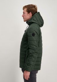 Donkergroen gewatteerd jack met een capuchon, voorzien van een gestikte structuur, elastische manchetten en een logo op de linkerarm. Ritszakken aan de zijkanten.