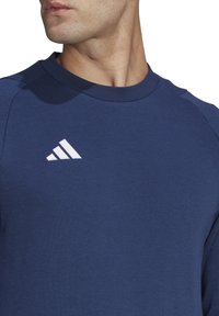 Marineblauwe sweatshirt met een ronde hals, voorzien van het witte Adidas-logo op de borst. Zachte textuur en raglanmouwen voor een relaxed fit.