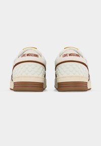 Ζευγάρι λευκά αθλητικά παπούτσια με καφέ λεπτομέρειες, υφή με μοτίβο καρδιών στη φτέρνα και το κείμενο "LOVE MOSCHINO" στην πίσω γλωττίδα.