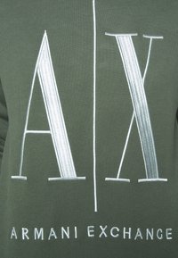 Zelená mikina s velkým vyšitým logem "AX" a textem "ARMANI EXCHANGE" v bílé barvě. Hladký materiál s klasickým střihem.