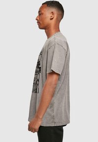 Gray oversized cotton t-shirt features a graphic print on the front, short sleeves, and a relaxed fit. The fabric has a textured, worn look.