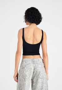 Zwarte geribbelde crop top met brede bandjes, gecombineerd met lichtgrijze jeans met slangenprint met een hoge taille en twee achterzakken.