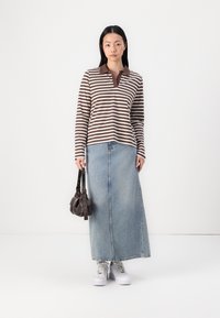 Brown and white striped long-sleeve top with a brown collar, paired with a light blue denim maxi skirt, white sneakers, and a small dark handbag.