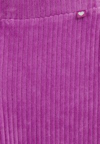 Violetti ribattu kangas, jolla on pehmeä ja pörröinen tekstuuri. Pienen sydänkuvioinnin omaava etiketti on näkyvissä yläkulmassa.