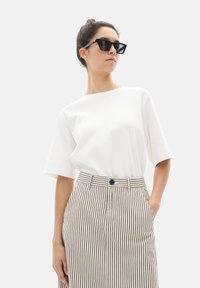 Un haut blanc à manches courtes associé à une jupe rayée taille haute beige et noire. La tenue présente une silhouette décontractée et des poches sur les côtés.