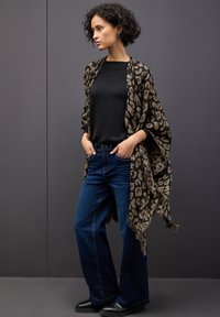 Leopardmönstrad sjal med fransade kanter, lager på en svart skjorta, matchad med blå vida jeans och svarta ankelstövlar.