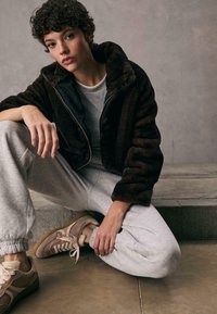 Faux fur brun jakke med høj krave, grå sweatshirt og grå sweatpants. Bæres med beige sneakers med lyse accenter.