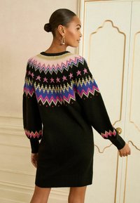 Rochie tricotată neagră, cu un model geometric colorat în roz, albastru și auriu pe yoke și manșete. Mâneci lungi, tip balon.