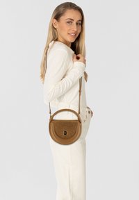 Bruine leren crossbody tas met een gestructureerd bovenstuk en cirkelvorm. Verstelbare schouderriem en accenten in goudkleurig metaal.