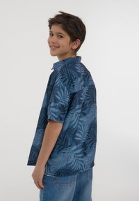 Camicetta a maniche corte in tonalità di blu con motivo a foglia. Realizzata in tessuto leggero, presenta un colletto e una vestibilità comoda.