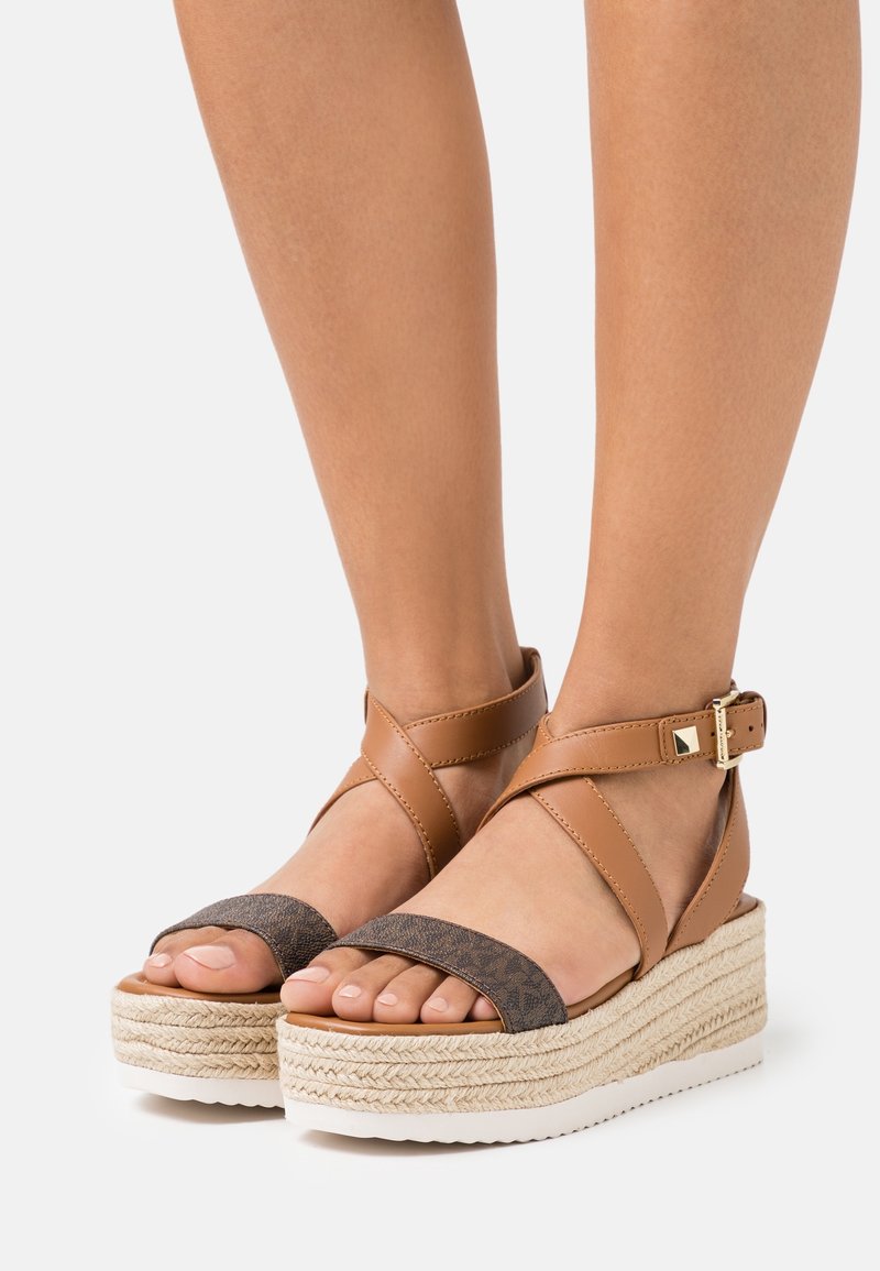 Sandales à plateforme en cuir marron avec semelle en jute tressé, bretelles croisées et tige en tissu sombre contrastant. Détail de boucle réglable à la cheville.