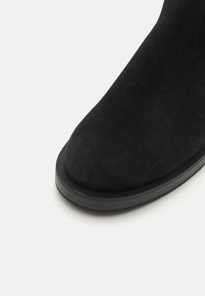 Zwarte suède enkellaars met een ronde neus, voorzien van een platte zwarte rubberen zool en een gladde textuur. Geen zichtbare patronen of hardwaredetails.