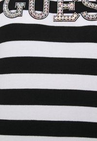 Haut en tricot rayé noir et blanc avec un grand lettrage "GUESS" orné de strass sur la poitrine pour un détail supplémentaire.