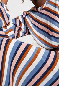 Robe rayée multicolore avec des rayures allongées en rose, bleu, marine et orange. Tissu doux avec un col rond et des manches bouffantes.