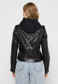 Černá kožená bunda s kapucí, přiléhavý střih, hladká textura, zipové manžety a zkrácená délka, doplněná o světle modré džíny.