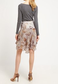 Kukkakuvioitu, kerroksittain leikattu vaaleanbeige hame, jossa on ruskeita ja vaaleanpunaisia yksityiskohtia, kerroksittain läpikuultavaa kangasta. Yhdistetty ruskeisiin, korkeakorkoisiin sandaaleihin.