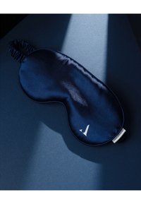 Granatowa satynowa maska na oczy do spania o zaokrąglonym kształcie, z elastyczną opaską i małym białym logo. Gładka faktura z połyskującą powierzchnią.