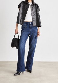 Svart kort jacka, vit topp, vida blå denimjeans med framfickor, samt spetsiga svarta klackskor, i kombination med en svart handväska.