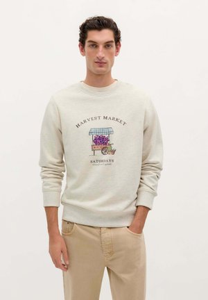 Lichtgrijs sweatshirt met een ronde hals, met een geïllustreerd ontwerp van een oogstmarkt met druiven en een kraampje. Gecombineerd met beige broek.