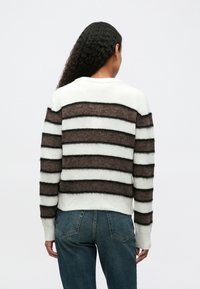 Maglione a righe con bande marroni e bianche, realizzato in materiale morbido. Presenta un collo rotondo e polsini a costine. Abbinato a jeans blu.