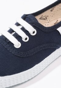 Zapatillas de lona en color navy con suela de goma blanca. Presentan cordones y costuras blancas, tela texturizada y diseño de puntera redondeada.