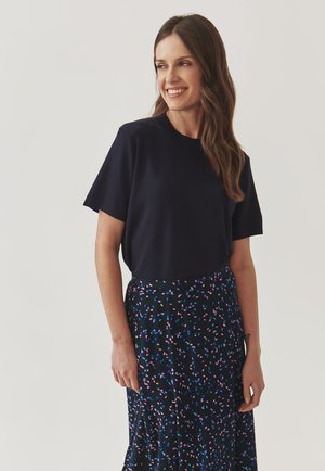 Navy short-sleeve top with a round neckline, paired with a patterned black skirt featuring multicolored leaf shapes in pink and blue.