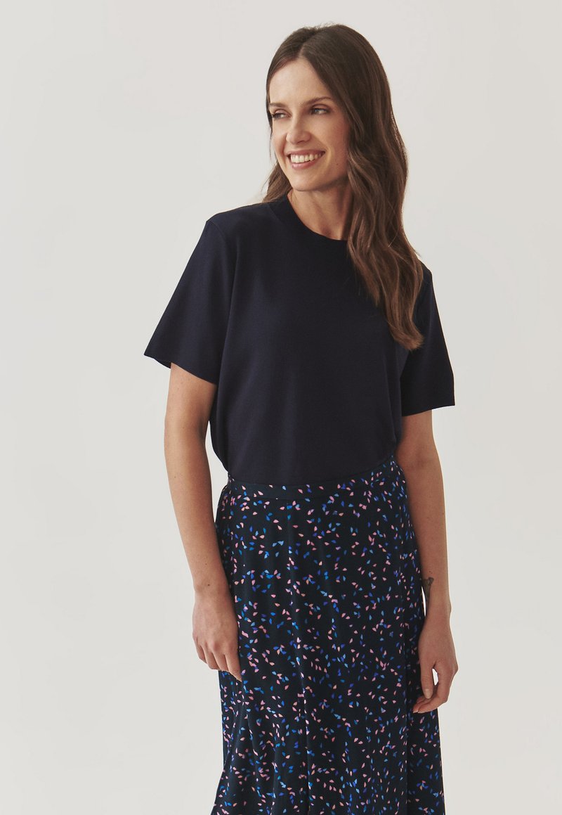Marineblauw kortemouwen top met een ronde halslijn, gecombineerd met een gestreepte zwarte rok met meerkleurige bladvormen in roze en blauw.