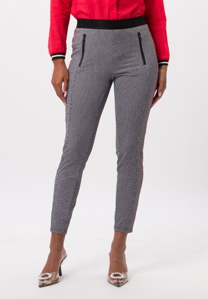 Pantalons slim en motif géométrique noir et blanc, dotés d'une taille élastique noire et de poches zippées sur les côtés, associés à des talons transparents à bouts pointus.