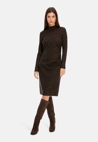 Langärmliges, enganliegendes Kleid in Dunkelbraun mit einem Zickzackmuster, ausgestattet mit einem hohen Kragen und einer Länge bis zur Mitte der Wade, kombiniert mit knielangen braunen Wildlederstiefeln.