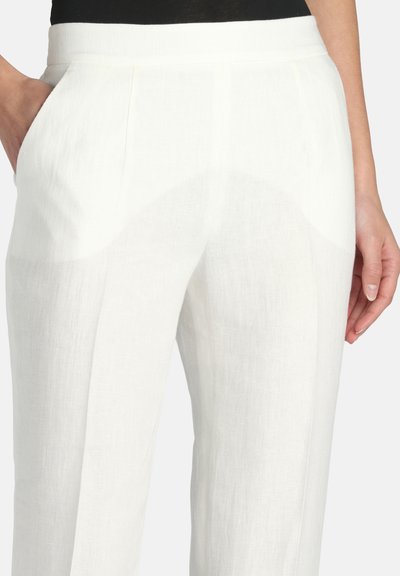 Fehér magas derekú lenvászon nadrág oldalzsebekkel, fekete felsővel viselve, a kezek lazán az oldaluk mellett.