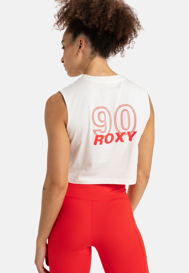 White cropped tank top with orange "90 Roxy" graphic on the back, paired with red high-waisted leggings. Soft cotton material, sleeveless design.