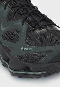 Čierna a šedá turistická obuv s textúrovaným syntetickým zvrškom s brandingom Gore-Tex, vystuženými akcentmi a polstrovanou podrážkou.