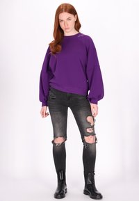 Lilla oversized sweatshirt med ribbede manchetter og inderklædning, parret med sorte slidte skinny jeans og sorte ankelstøvler.