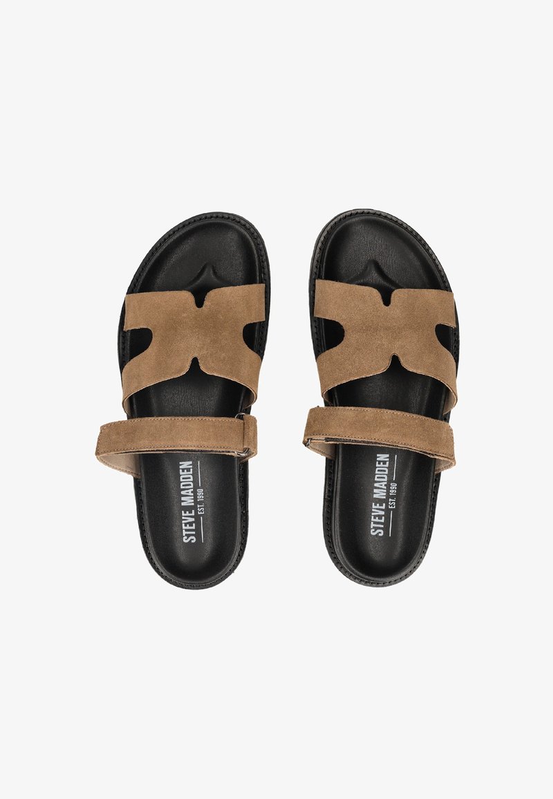 Sorte skyggesandaler med brune ruskinds krydsede remme og justerbare ankelremme, mærket med "Steve Madden" på fotsengene.