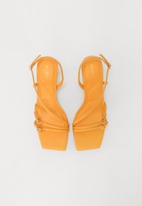 Sandales à talons hauts jaunes à lanières avec un design à bout carré, présentant deux fines lanières de cheville et une boucle réglable.