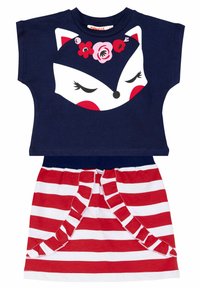 Niebieska bluzka z krótkim rękawem z białym wzorem twarzy lisa z kwiatowymi akcentami; w połączeniu z czerwoną i białą spódnicą w paski z falbanami.