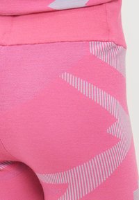 Ružové legíny s tkanými geometrickými vzormi, ktoré obsahujú jednofarebné a pruhované dizajny v kontrastných odtieňoch, vyrobené z mäkkého, elastického materiálu.