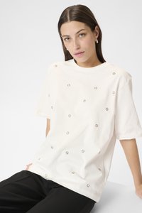 Tricou alb cu mânecă scurtă, cu accente metalice circulare pe partea din față. Material moale, croială relaxată, guler rotund, asortat cu pantaloni negri.