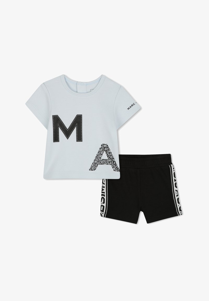 T-shirt azzurro chiaro con maniche corte, caratterizzato da una grande "M" nera e disegni "A" a motivi; abbinato a pantaloni corti neri con strisce bianche sui lati.