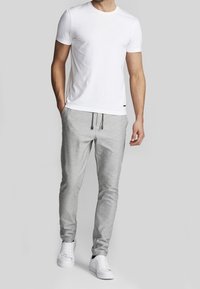 T-shirt blanc à manches courtes associé à un pantalon de jogging gris clair avec une taille élastique et un cordon, complété par des baskets blanches.