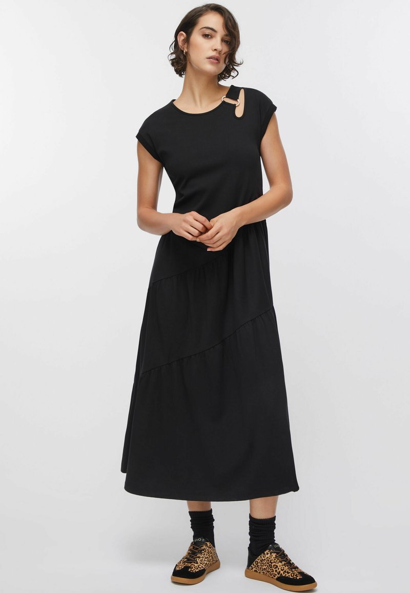 Robe midi noire avec un col rond et des manches courtes, présentant des volants superposés et un accent distinctif en clip or rose.