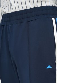 Navyfarbene Sport-Jogginghosen mit elastischem Bund, seitlichen Taschen und kontrastierenden weißen Streifen. Auf dem Oberschenkel befindet sich ein kleines hellblaues Logo.