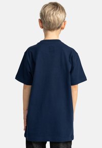 Mörkblå bomullströja med korta ärmar, avslappnad passform och en liten logotag på baksidan av halsringningen. Mjuk textur och enkelt design.