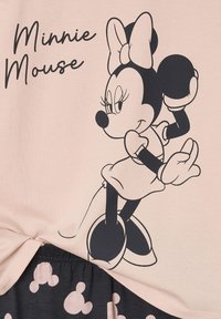 Light pink t-shirt featuring a black outline of Minnie Mouse, with a bow, on top of dark fabric displaying repeating mouse silhouettes.