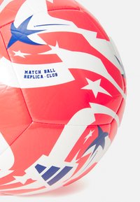 Rød og hvid fodbold med stjerne- og swoosh-mønstre, der har teksten "MATCH BALL REPLICA-CLUB" i blå. Tekstureret overflade, hexagonale paneler.