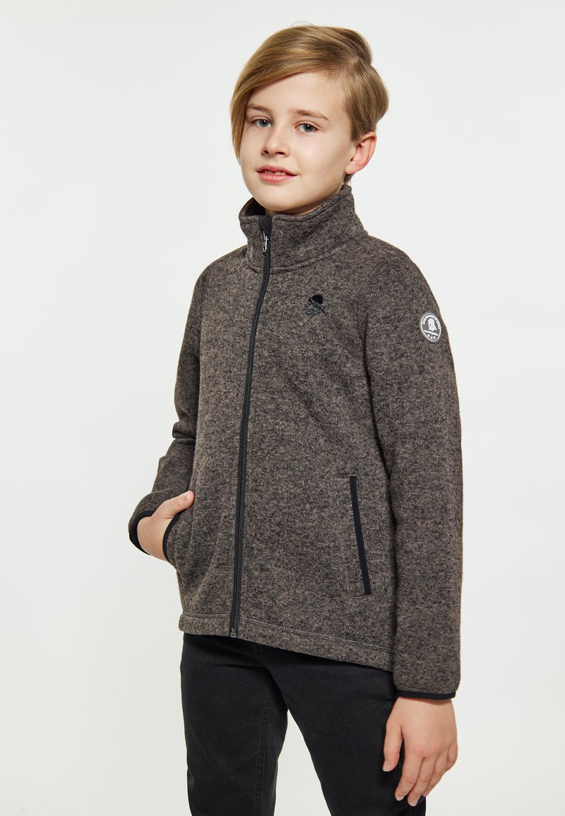 Giacca in pile di colore grigio scuro con colletto alto, zip frontale e tasche laterali. Presenta una toppa con logo sul braccio sinistro e rifiniture nere sui polsini.