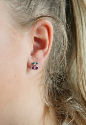 Zilveren kersenstuds met twee ronde paarse stenen en groene accenten, gepositioneerd tegen de achtergrond van een mensenoor en haar.
